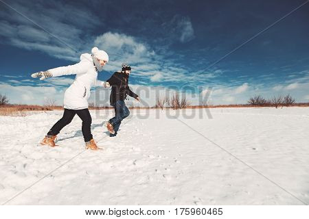 Concept of happy family life, winter holidays, hike. girlfriend ans boyfriend runnning on snowy field over beautiful blue sky background