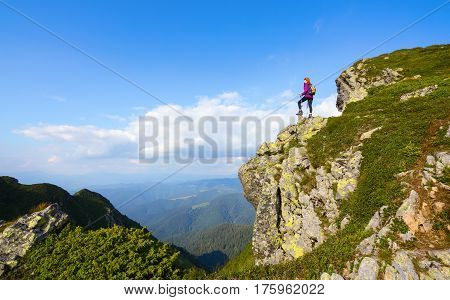 Sporty girl with back sack is standing at the edge of the precipice and watching on the endless vast of mountains landscape in the sunny day.