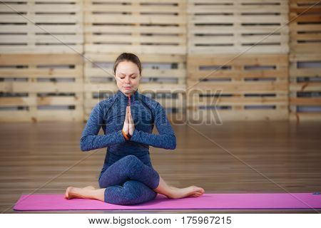 Young attractive woman practicing yoga, exercise, Lotus pose, namaste, working out, wearing blue sportswear. Sitting on the pink yoga mat. In gym. Health lifestyle.