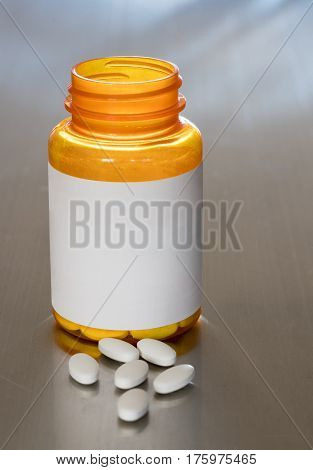 Prescription bottle with blank label for copy space and white pills or tablets on metal table for opioid epidemic illustration