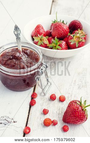 Homemade delicious strawberry jam in a glass jar and fresh strawberries on white rusric wooden background. Selective focus.