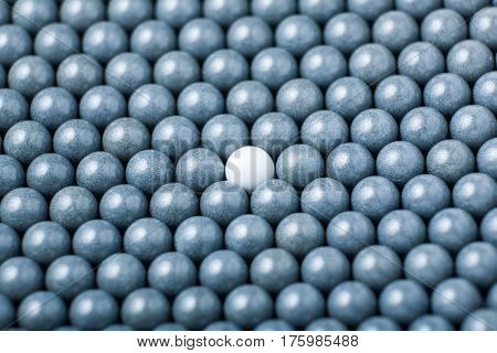 White Airsoft Ball Is Among Many Black Balls. Background Of 6Mm Bbs