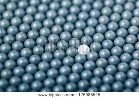 White Airsoft Ball Is Among Many Black Balls. Background Of 6Mm Bbs