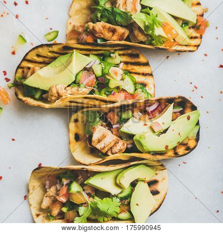 Healthy corn tortillas with grilled chicken, avocado, fresh salsa, limes over light grey marble background, top view, square crop. Healthy food, gluten-free, allergy-friendly, weight loss concept