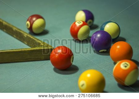 Multicolored Blurred Billiard Balls With Numbers Are On The Table With Blue Cloth And Wooden Pyromid