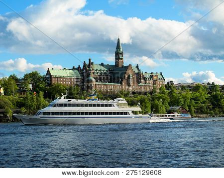 Tourist Cruise Boat Floats On The Blue Water Of The Lake On The Background Of The Beautiful Building