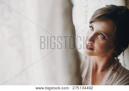 Beautiful Stylish Brunette Bride Posing In Silk Robe Near Wedding Gown In The Morning. Sensual Portr