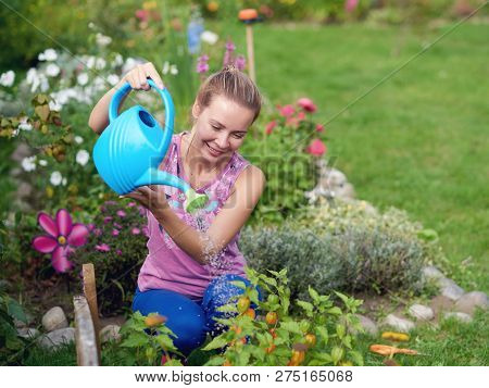 Smiling Caucasian Woman Watering Plants With Water Can On A Croft.