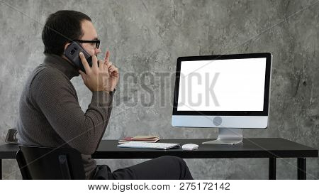 Male Designer Working At Computer In Contemporary Office. He Talks On The Phone And Looking On What 