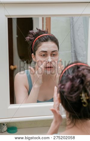 Attractive Girl Uses Facial Scrub Looking In The Mirror.