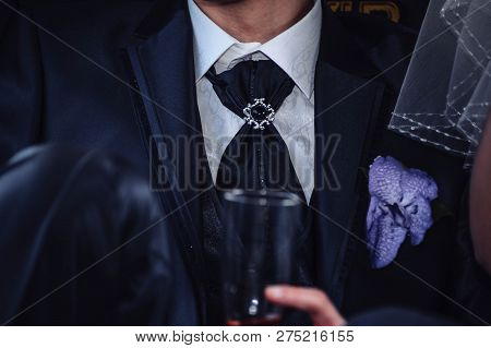 The Groom In A Beautiful Tie And With A Glass Of Champagne Sits Next To The Bride