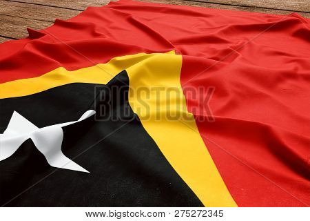 Flag Of East Timor On A Wooden Desk Background. Silk East Timorese Flag Top View.