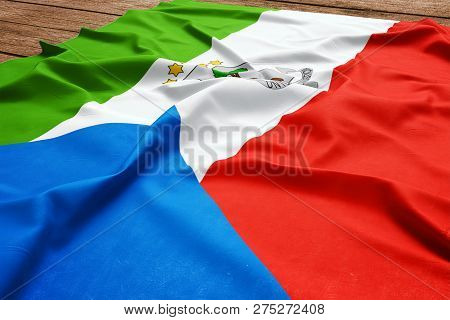 Flag Of Equatorial Guinea On A Wooden Desk Background. Silk Equatoguinean Flag Top View.