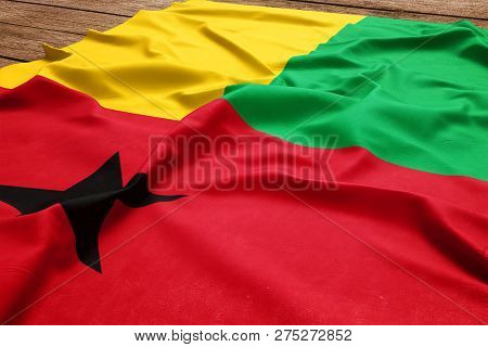 Flag Of Guinea Bissau On A Wooden Desk Background. Silk Flag Top View.