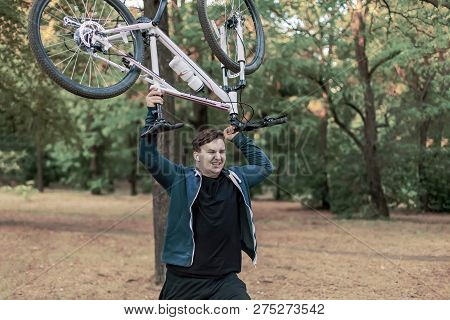 Young Emotional Cuacasian Man Crashes The Bicycle Holdlnig It Up In Both Hands, Angry Expression On 