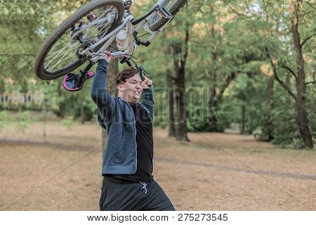 Young Emotional Cuacasian Man Crashes The Bicycle Holdlnig It Up In Both Hands, Angry Expression On 