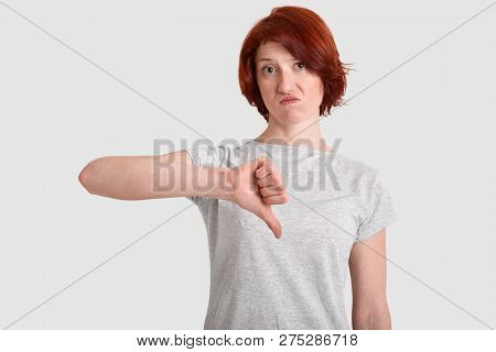 Displeased Red Haired Woman Keeps Thumb Down, Frowns Face, Doesnt Like Something, Dressed In Casual 