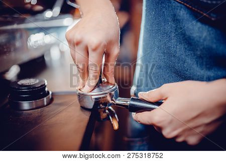 Close Up Of Bartender In Blue Apron Tempering Ground Coffee To Make Morning Hot Cappuccino Drink. Wo