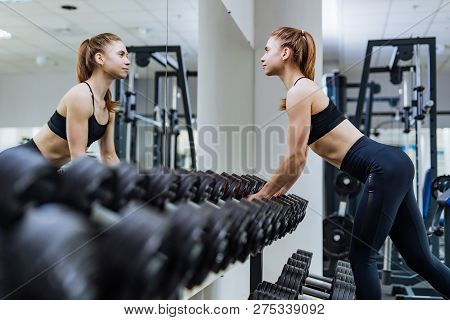 Sexy Fitness Girl Taking Dumbbells In Front Of The Mirror In The Sport Gym. Slim, Bodybuilder Girl, 