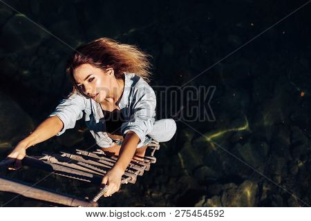 Ambition Wings Her Spirit. Sexy Woman Climbing Up Rope Ladder. Sensual Woman Hang On Rope Over Water