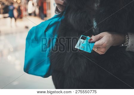 Well-dressed Lady In Fur Holding Credit Card And Bag At Blurred Mall Background. Woman Paying In Fas