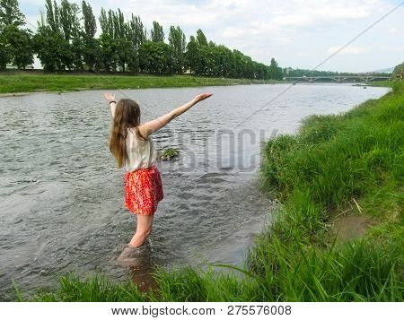 Adult Girl With Long Blond Hair Splashes In The Water Of Uzh River - Back View. A Young Woman Enjoys