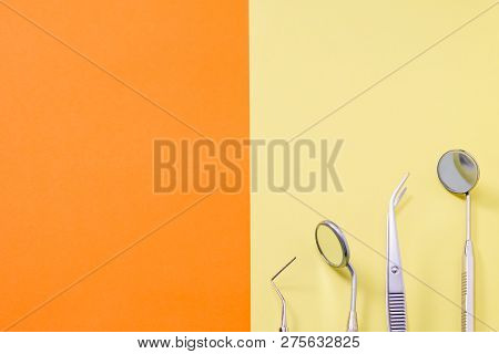 Dentist Tools: Two Mirrors, Explorer And Tweezers On Orange Yellow Bacrground With Copy Space.