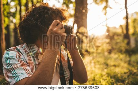 Horizontal Side View Of Handsome Male With Curly Hair Taking Photos Of Nature On His Digital Camera.