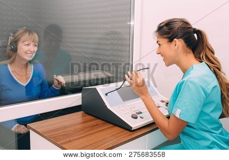 Audiologist Doing Hearing Exam To A Mature Patient Using Audiometer In Special Audio Room.