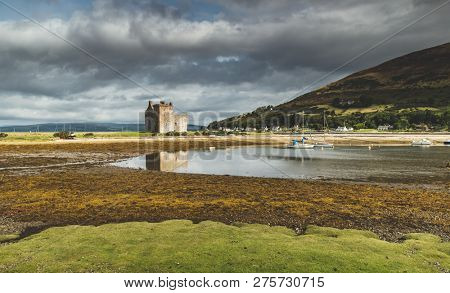 Lochranza castle next to the Arran island bay. Scotland. Amazing countryside landscape. Ancient building on the Scottish shoreline. Autumn scene. Grey cloudy sky before the rain.