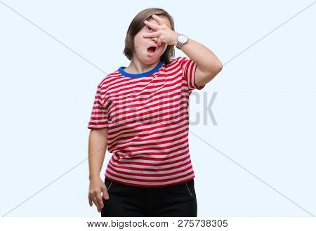 Young adult woman with down syndrome over isolated background peeking in shock covering face and eyes with hand, looking through fingers with embarrassed expression.