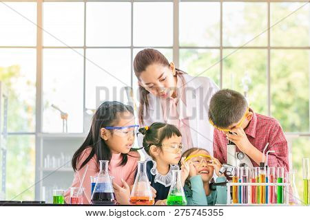 Science Teacher Teach Asian Students In Laboratory Room, Boy  Look Through Microscope, Colorful Test