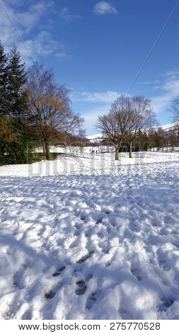 People Playing In The Distance On A Snowy Day In The Peak District, Derbyshire, With Trees, Sun And 