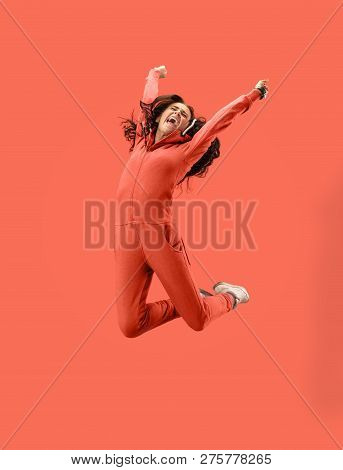 Freedom In Moving. Mid-air Shot Of Pretty Happy Young Woman Jumping And Gesturing Against Coral Stud