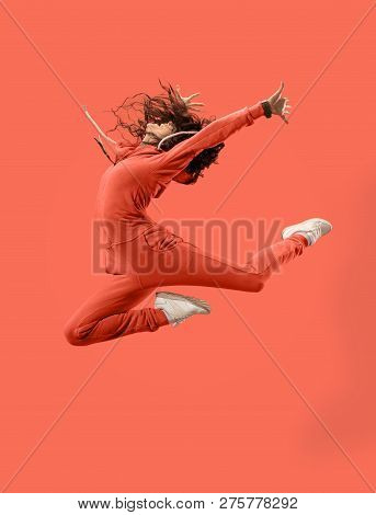 Freedom In Moving. Mid-air Shot Of Pretty Happy Young Woman Jumping And Gesturing Against Coral Stud