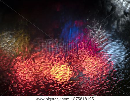 Abstract Pattern Of Colorful Lights And Rain Drops During Downpour On Winshield Of Car After Dark