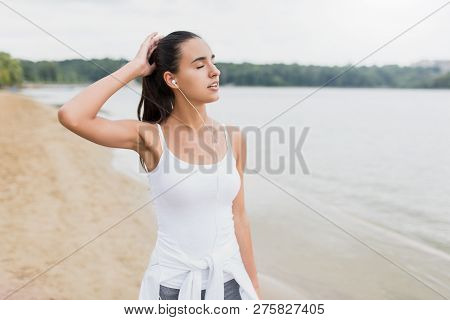 Beautiful Fit Female Athlete Girl On Beach Of Lake In Park. Listen And Enjoy The Music On Her Earpho