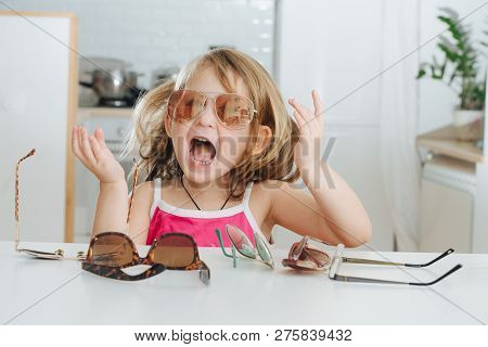 Portrait Of Cute Dark Blonde Little Girl With Short Hair Trying To Wear Pinhole Glasses. She Is At H