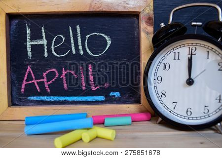 Hello April. Back To School Concept. Alarm Clock On Wooden With Blackboard On Background