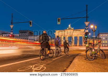 Backside Of The Brandenburg Gate At Night. Cyclists Are Waiting At The Traffic Light. Passing Cars I