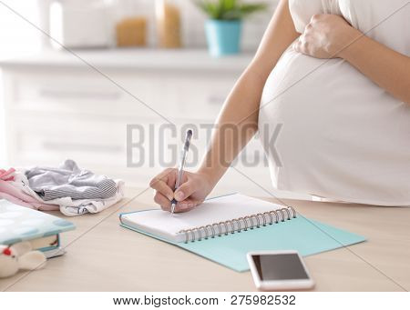 Pregnant Woman Writing Packing List For Maternity Hospital In Kitchen, Closeup