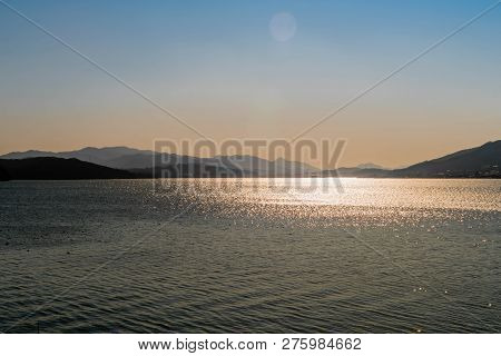 Sunshine Glimmering On Yedang Reservoir During Blue Hour With Mountains In Background. Located In Ye