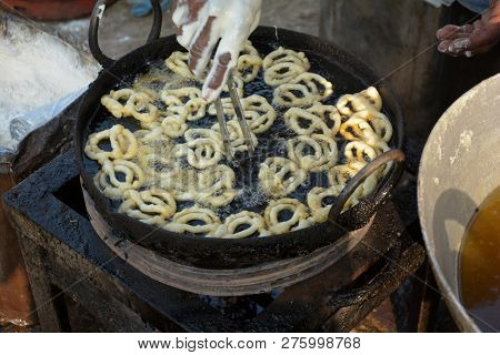 Close of a hand frying jalebi in hot oil in a street village market in a stove in daylight