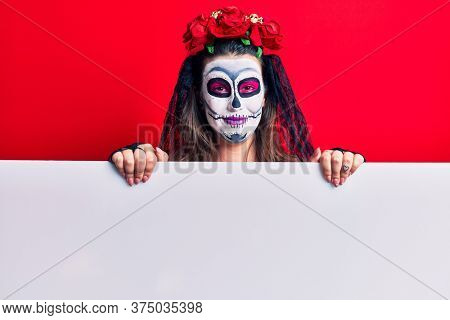 Young woman wearing day of the dead costume holding blank empty banner looking positive and happy standing and smiling with a confident smile showing teeth 