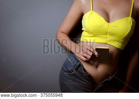 Young Woman Holding A Blackbox In Yellow Singlet And Jeans Texas Shorts On Dark Background.