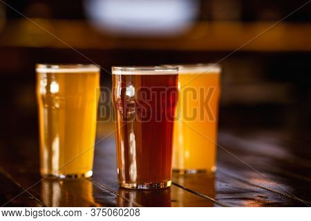 Beer Craft Style. Barley, Unfiltered, Light Drink In Glasses On Wooden Table In Blurry Interior Of P