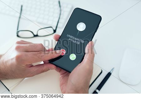 Close-up View Of Person Rejecting Call From Unknown Number With Text Unbekannter Anrufer, German For