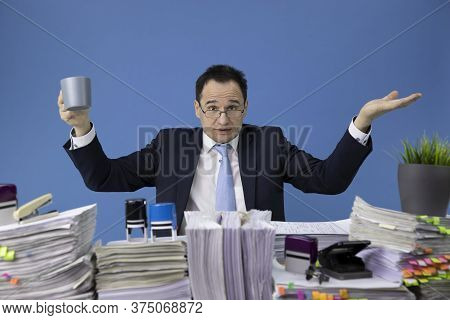 Outraged Businessman Waving His Hands Over Desk Full Of Documents. The Concept Of Overload And Busin