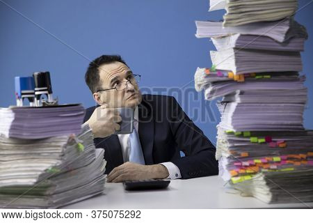 Exhausted Businessman Has Too Much Of Paperwork Looking At High Pile Of Documents In Fright. Fatigue