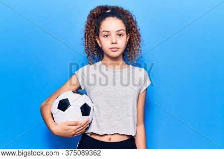 Beautiful kid girl with curly hair holding soccer ball thinking attitude and sober expression looking self confident 